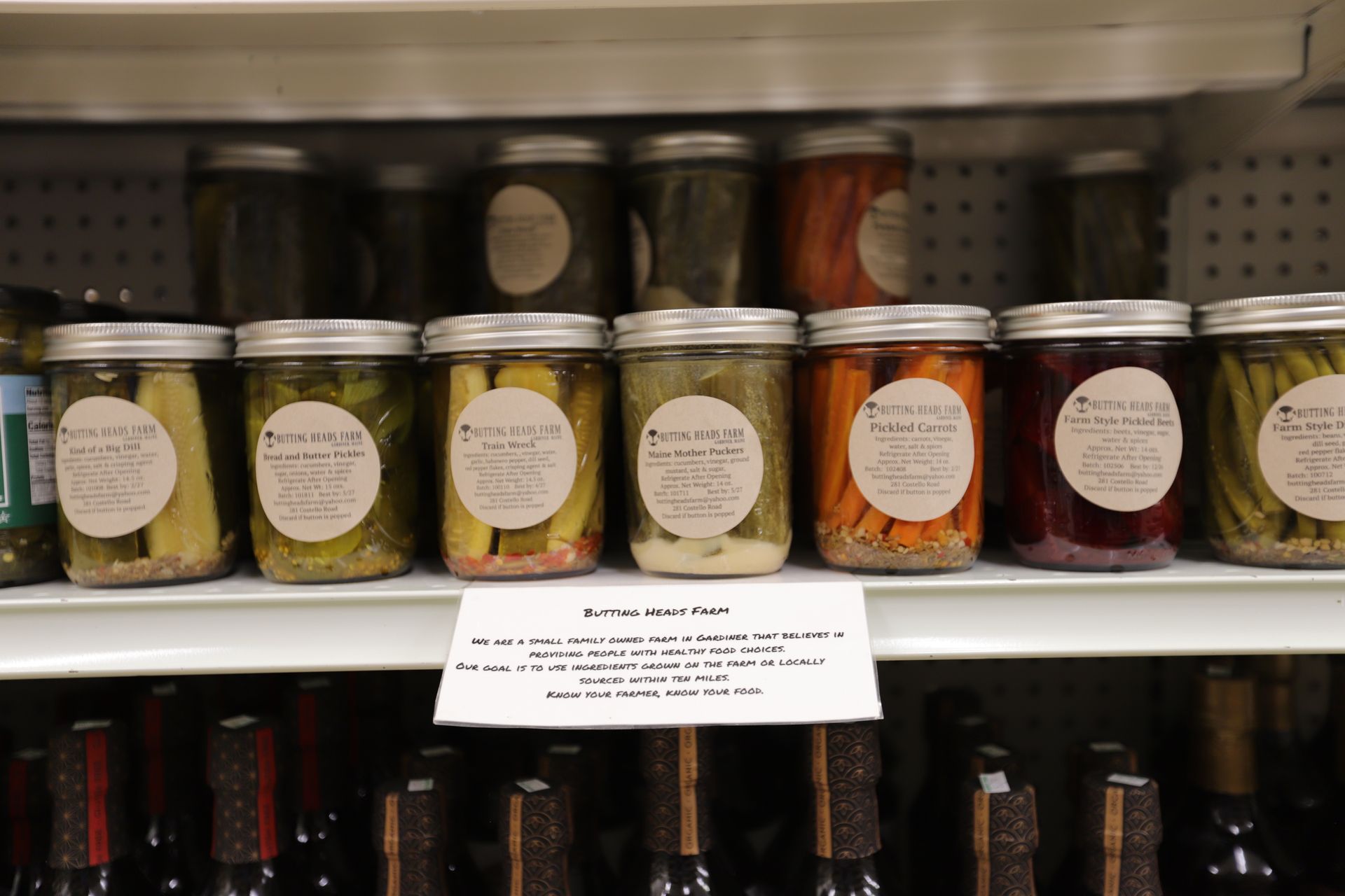 Store shelves filled with various glass jars of pickled vegetables and a price sign underneath.