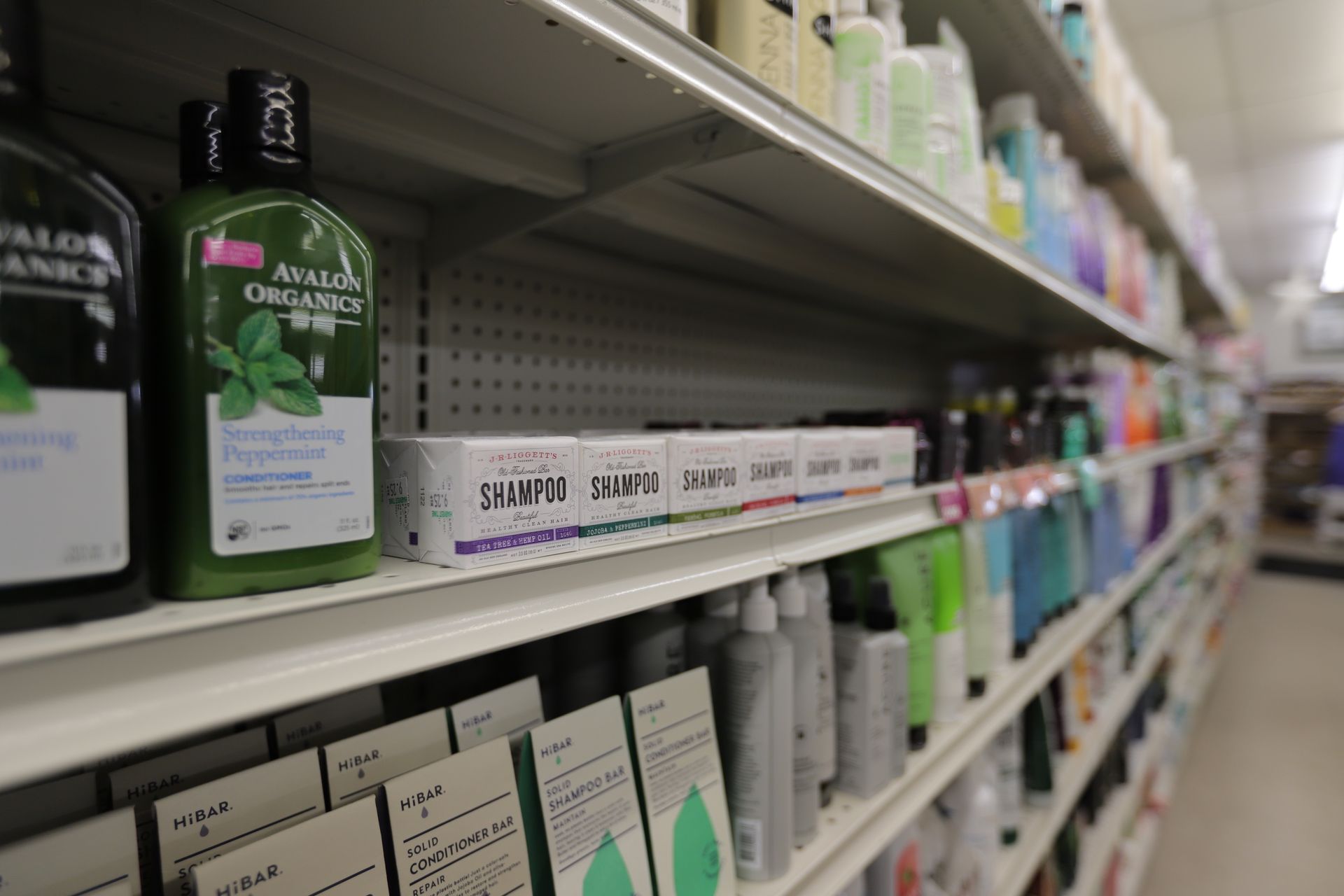 A store shelf displaying rows of hair care products, including Avalon Organics bottles and bars of shampoo.