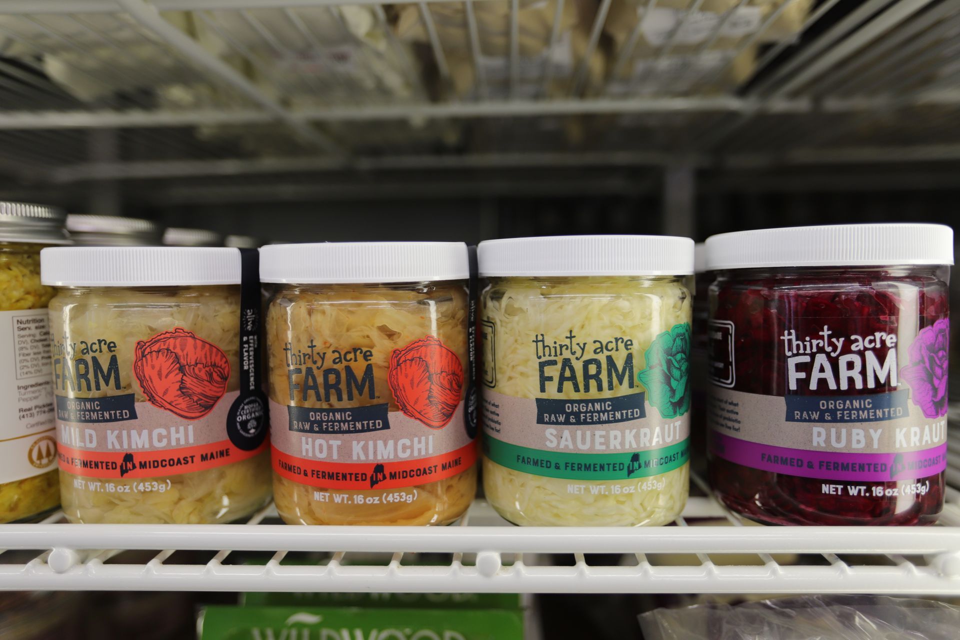 Four jars of Thirty Acre Farm fermented vegetables—kimchi, sauerkraut, and ruby kraut—lined up on a refrigerated shelf.