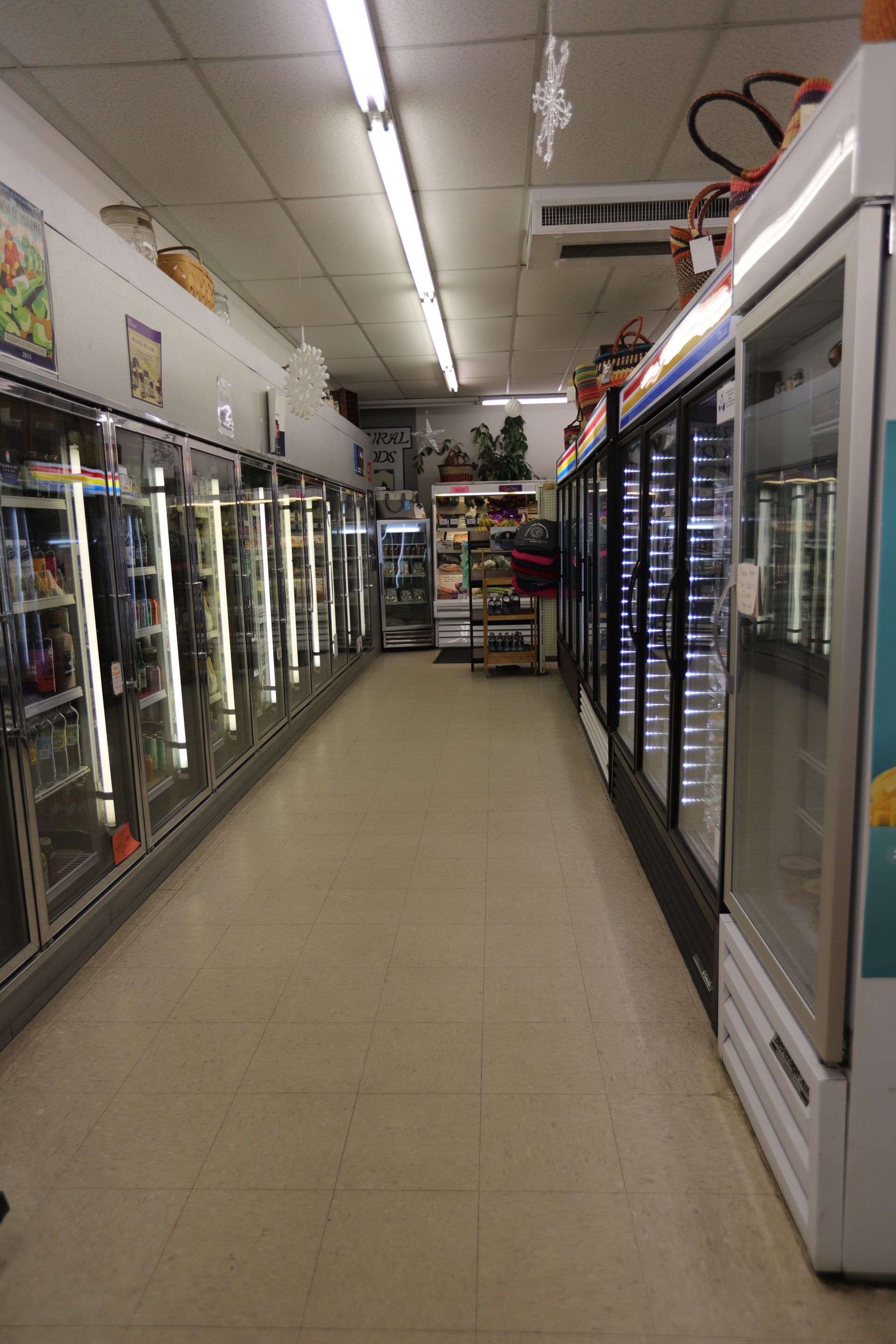A narrow aisle in a small store lined on both sides with glass-front commercial refrigeration units.