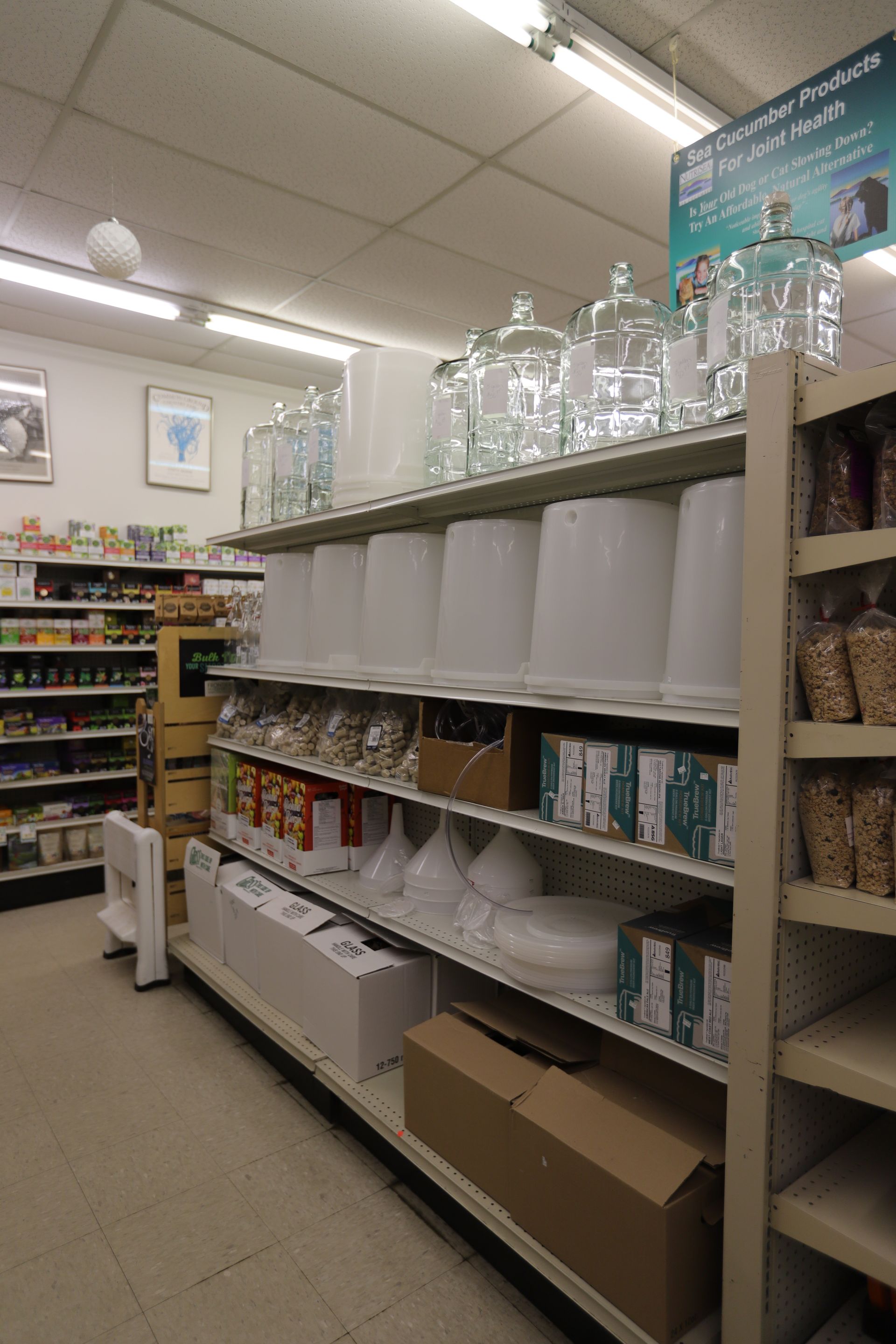 Shelves in a store aisle stocked with clear glass jars, white containers, white funnels, and boxes.