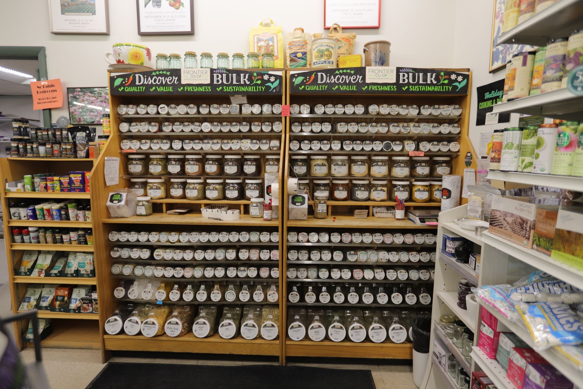 Wooden shelves in a store display numerous glass jars filled with various bulk spices, herbs, and dry goods.