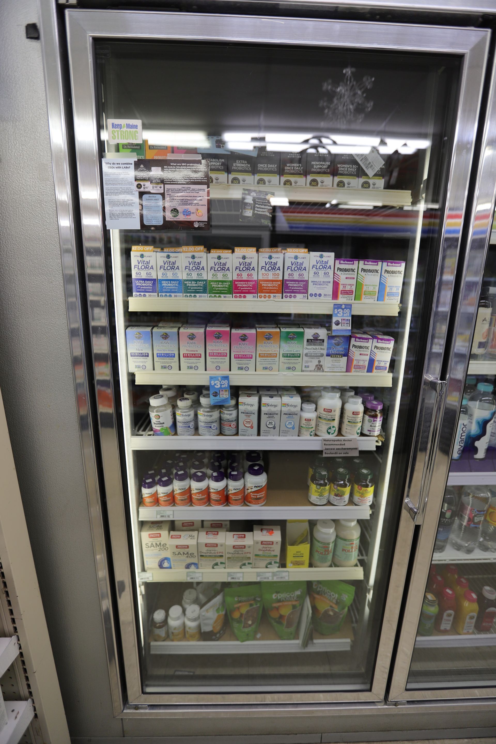A refrigerated display case in a store, stocked with rows of various milk cartons, bottled beverages, and packaged snacks.