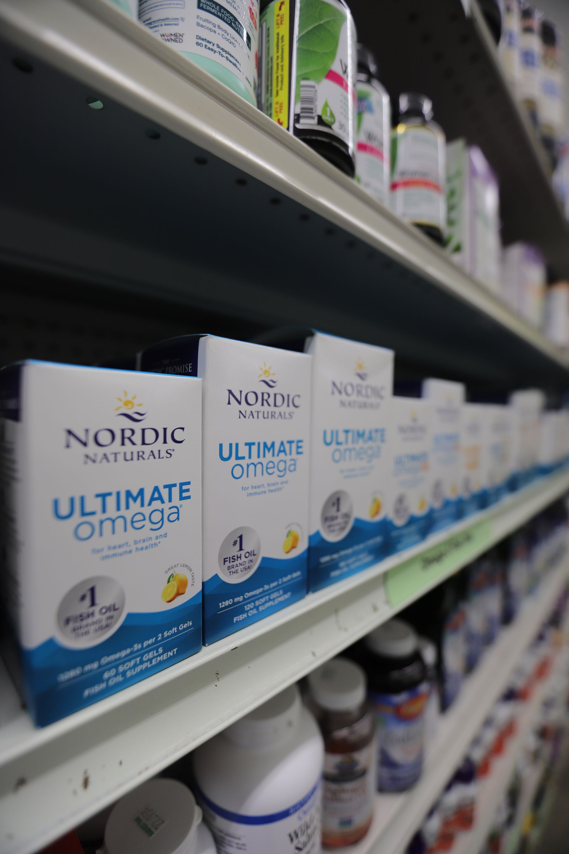 Shelves in a store stocked with Nordic Naturals Ultimate Omega supplement boxes and various bottles of vitamins.