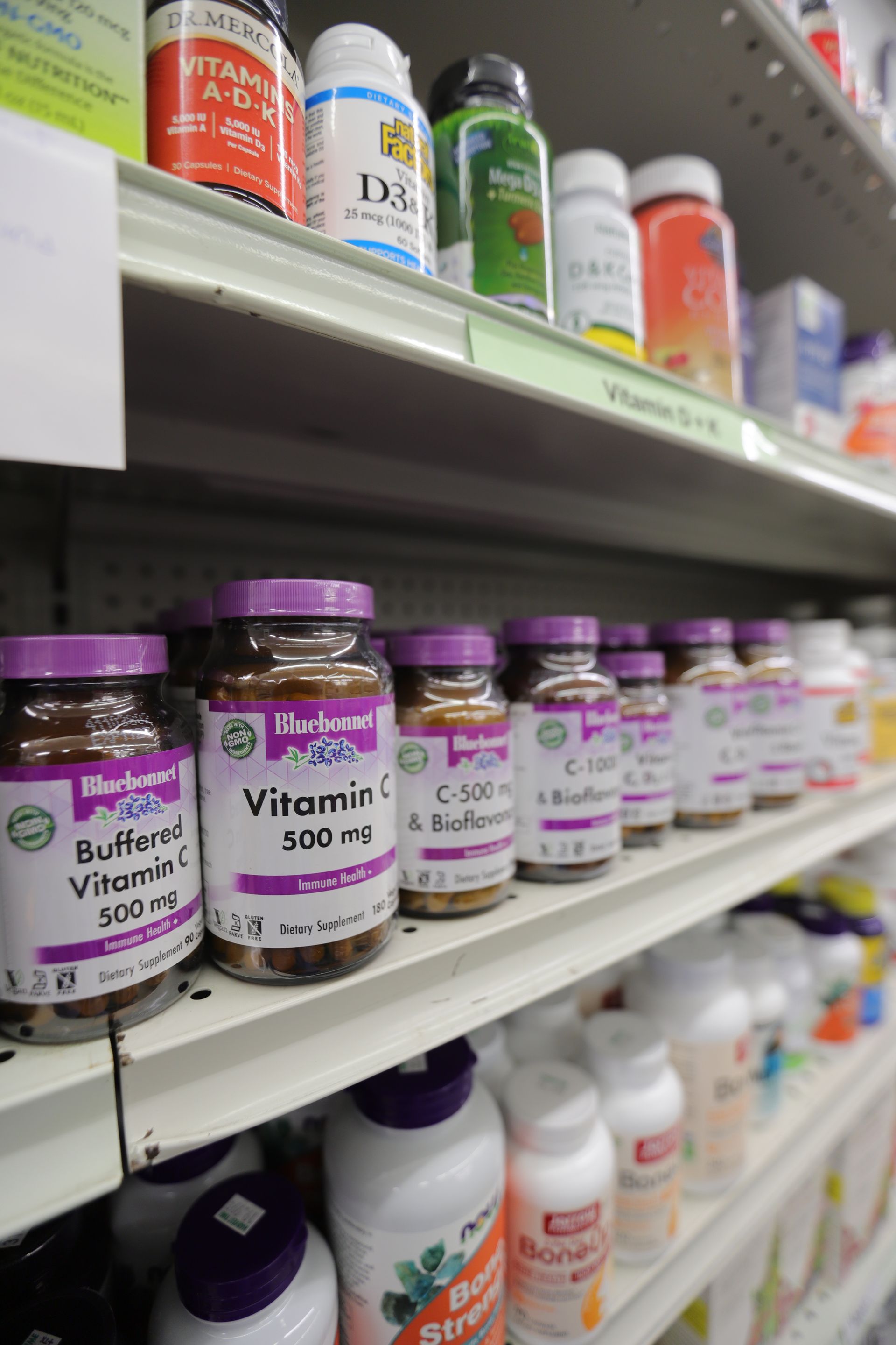 Store shelves stocked with rows of various vitamin and supplement bottles with purple and white labels.
