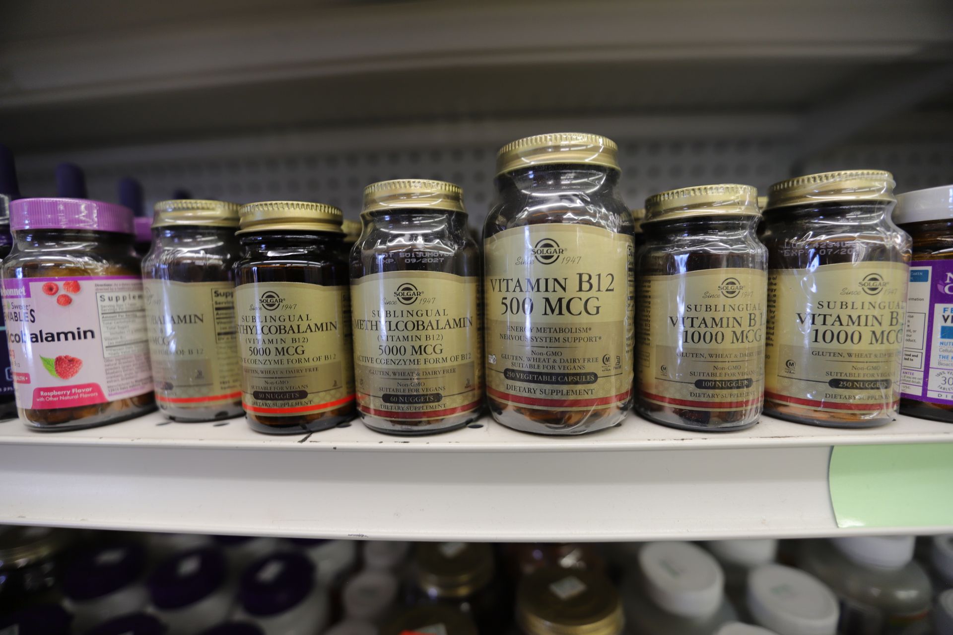 A shelf in a store displaying various bottles of vitamins and supplements with gold-colored labels.