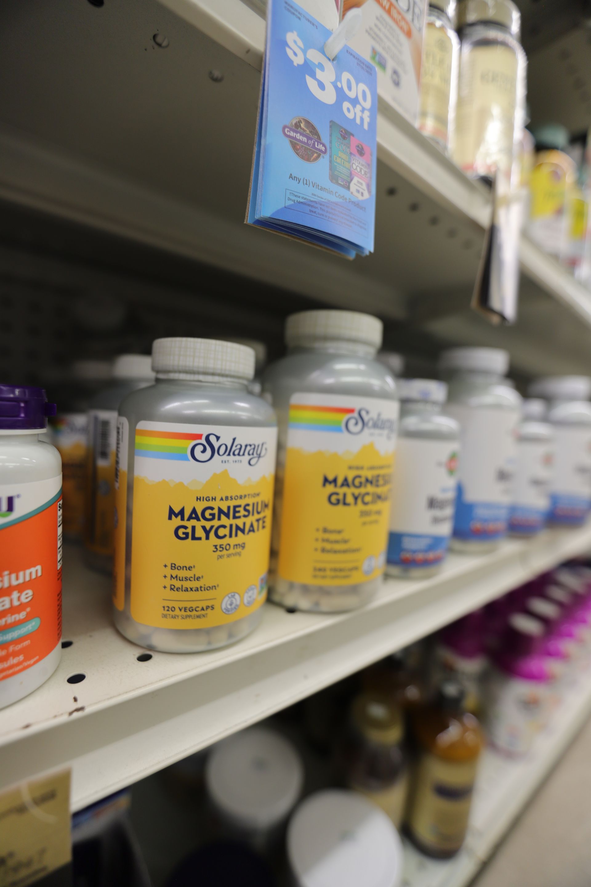 Solgar Magnesium Glycinate supplement bottles on a store shelf, with a $3.00 off sale sign hanging above.