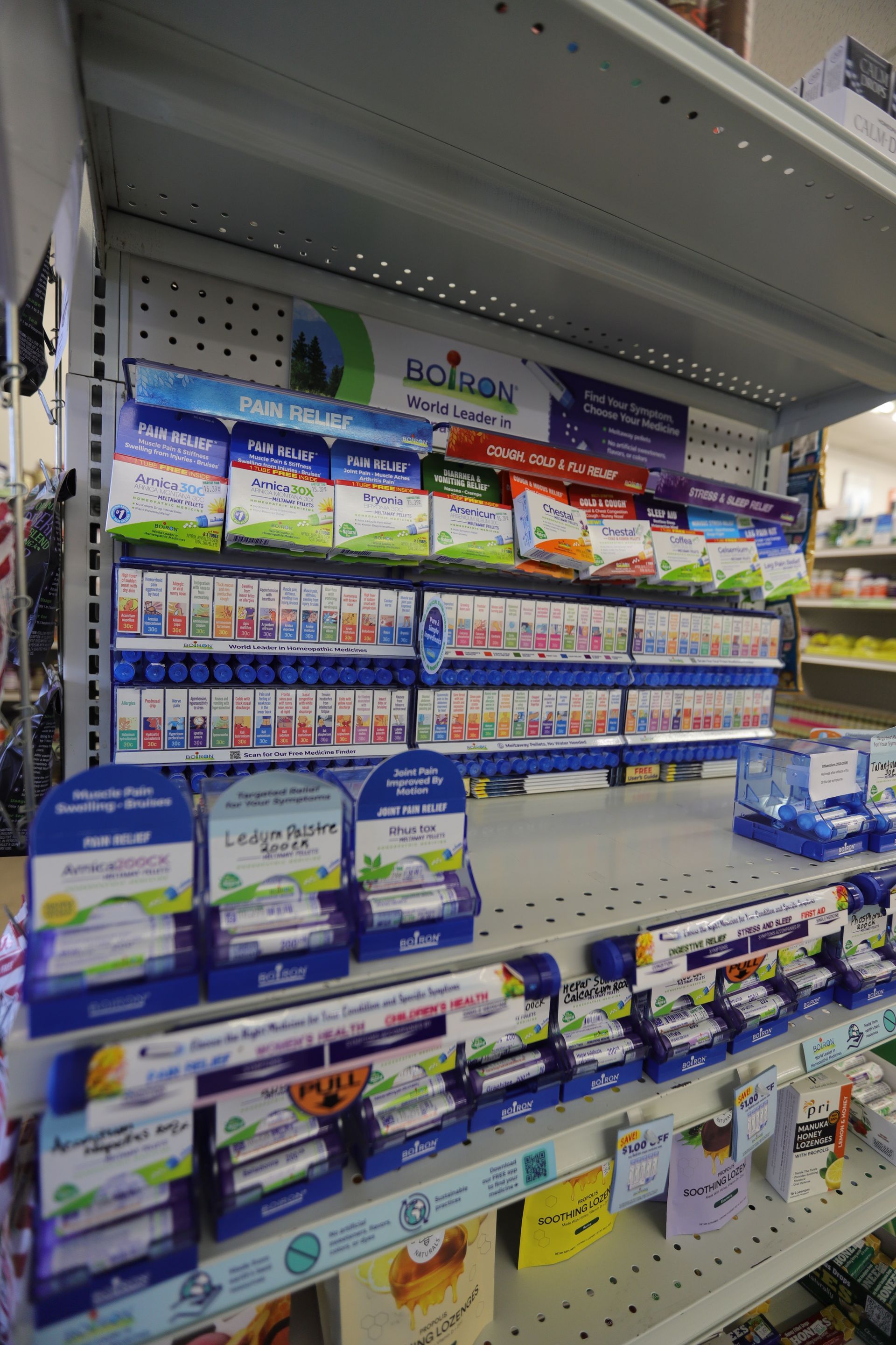 Store shelves stocked with various Boiron homeopathic medicine boxes, organized in blue displays.