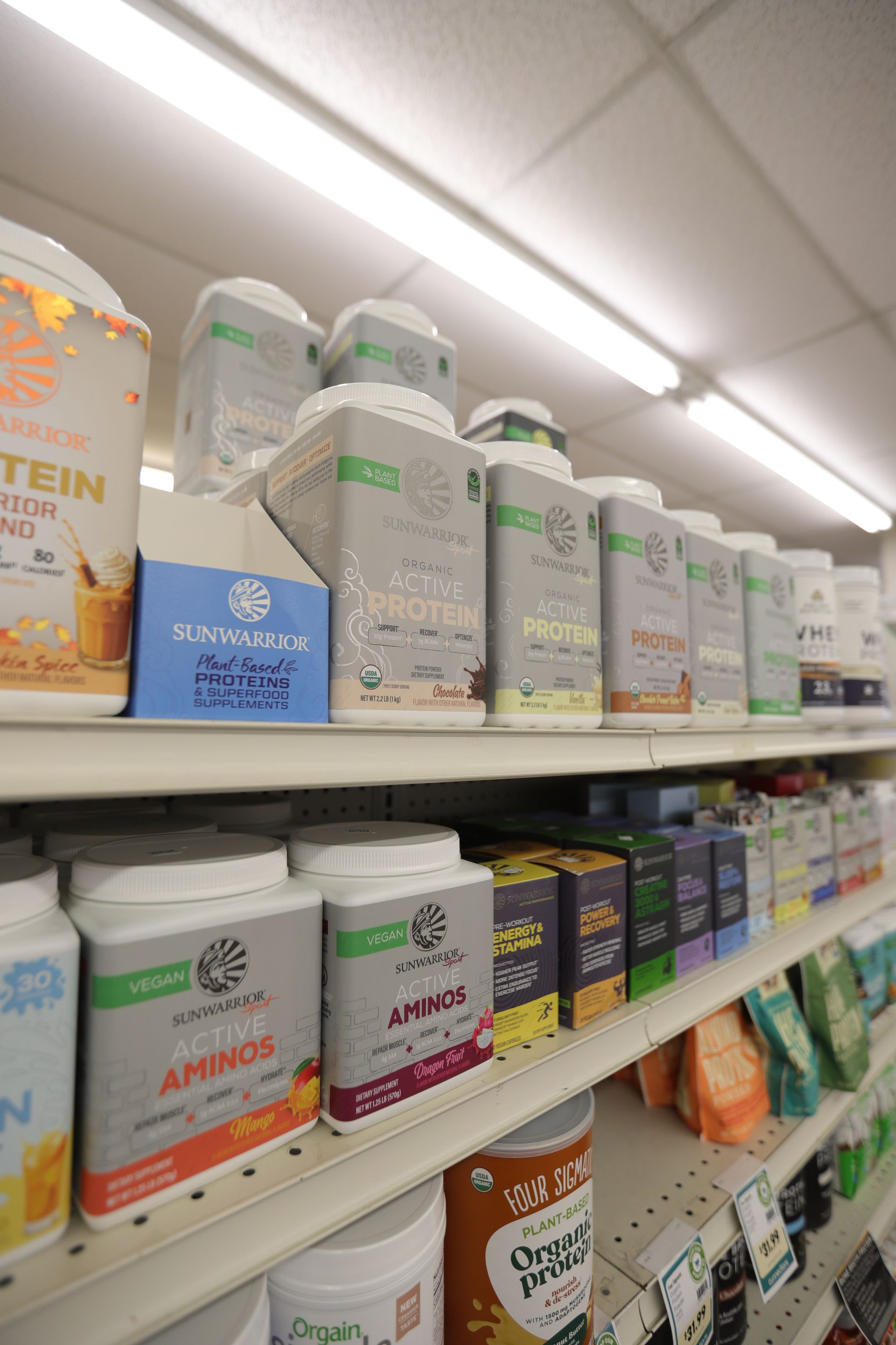 A retail store shelf stocked with rows of labeled plastic protein and supplement containers.