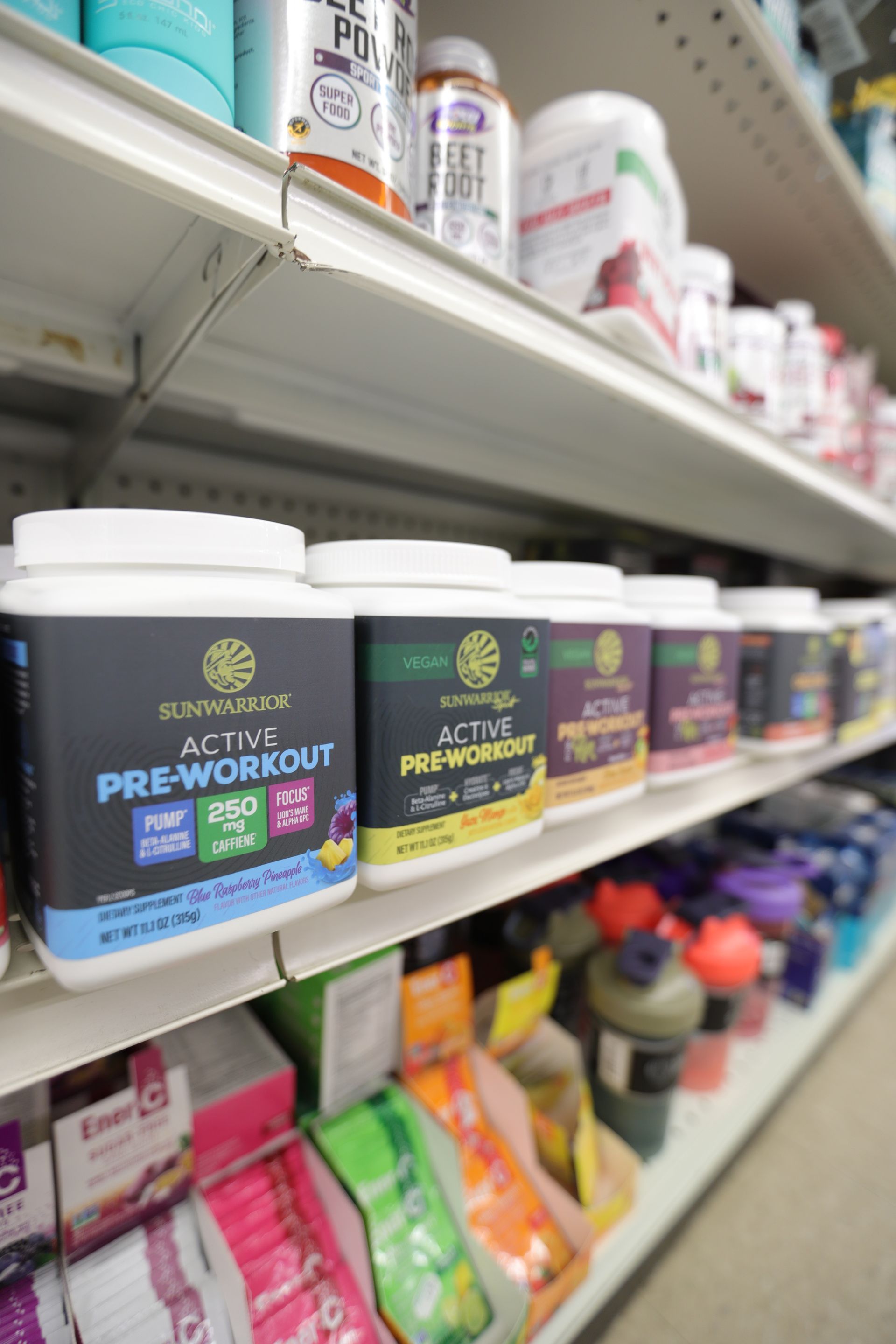 Shelves in a store displaying various dietary supplement containers and pre-workout powders in different colors.
