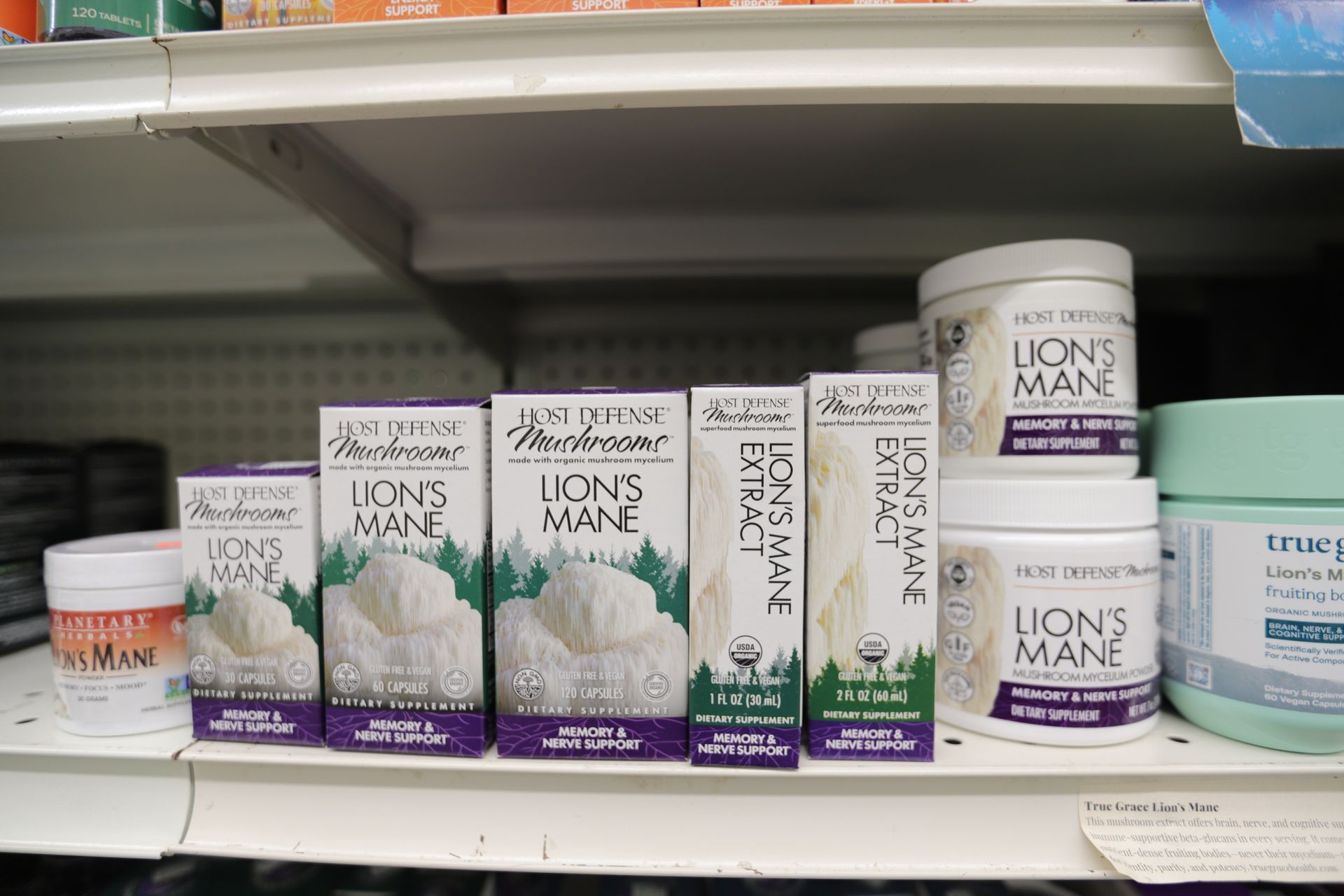 A store shelf displays various Host Defense Lion's Mane mushroom supplement boxes and jars.
