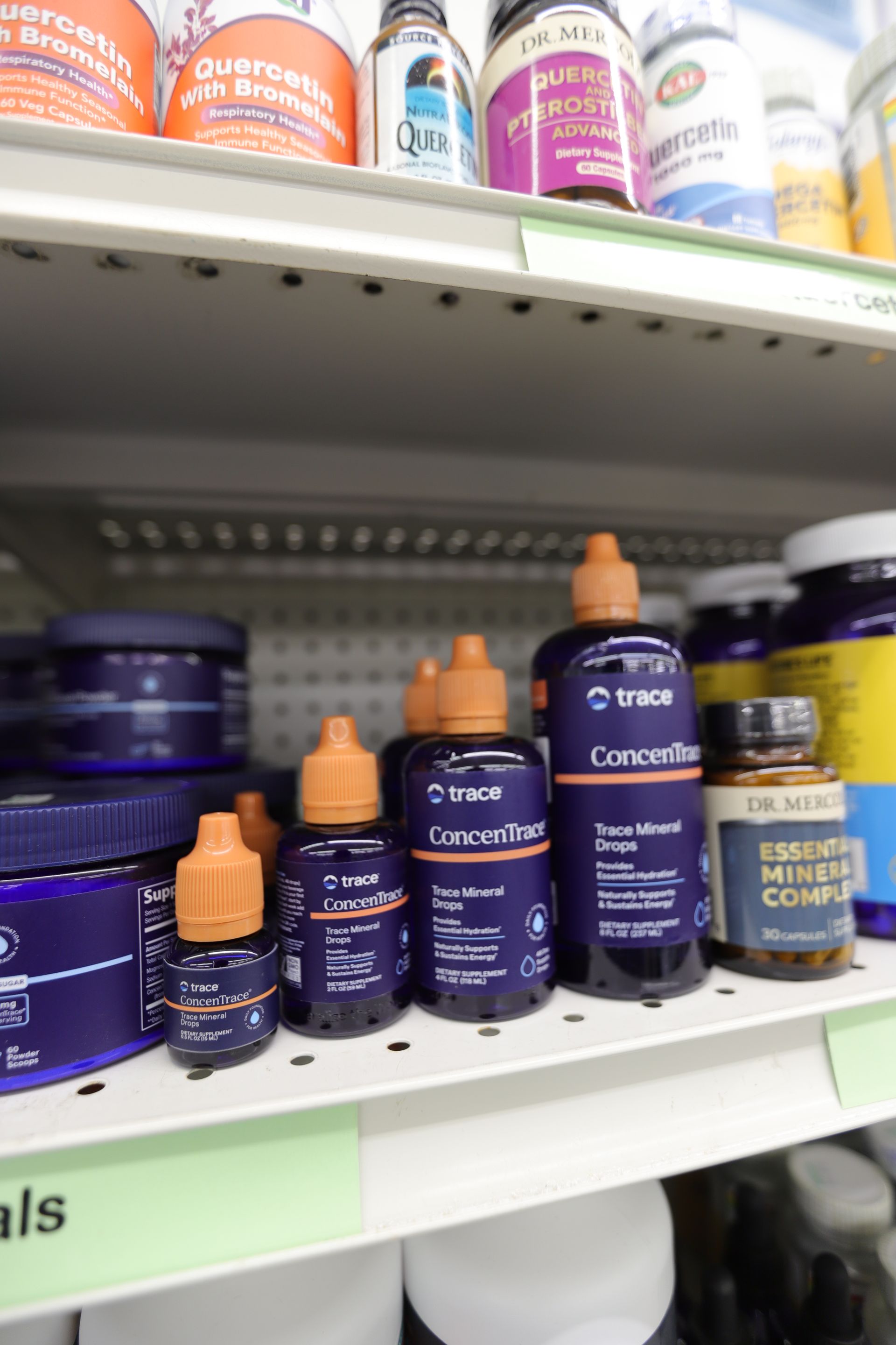 Store shelf with various supplement bottles, featuring several dark blue Trace Minerals dropper bottles in the center.