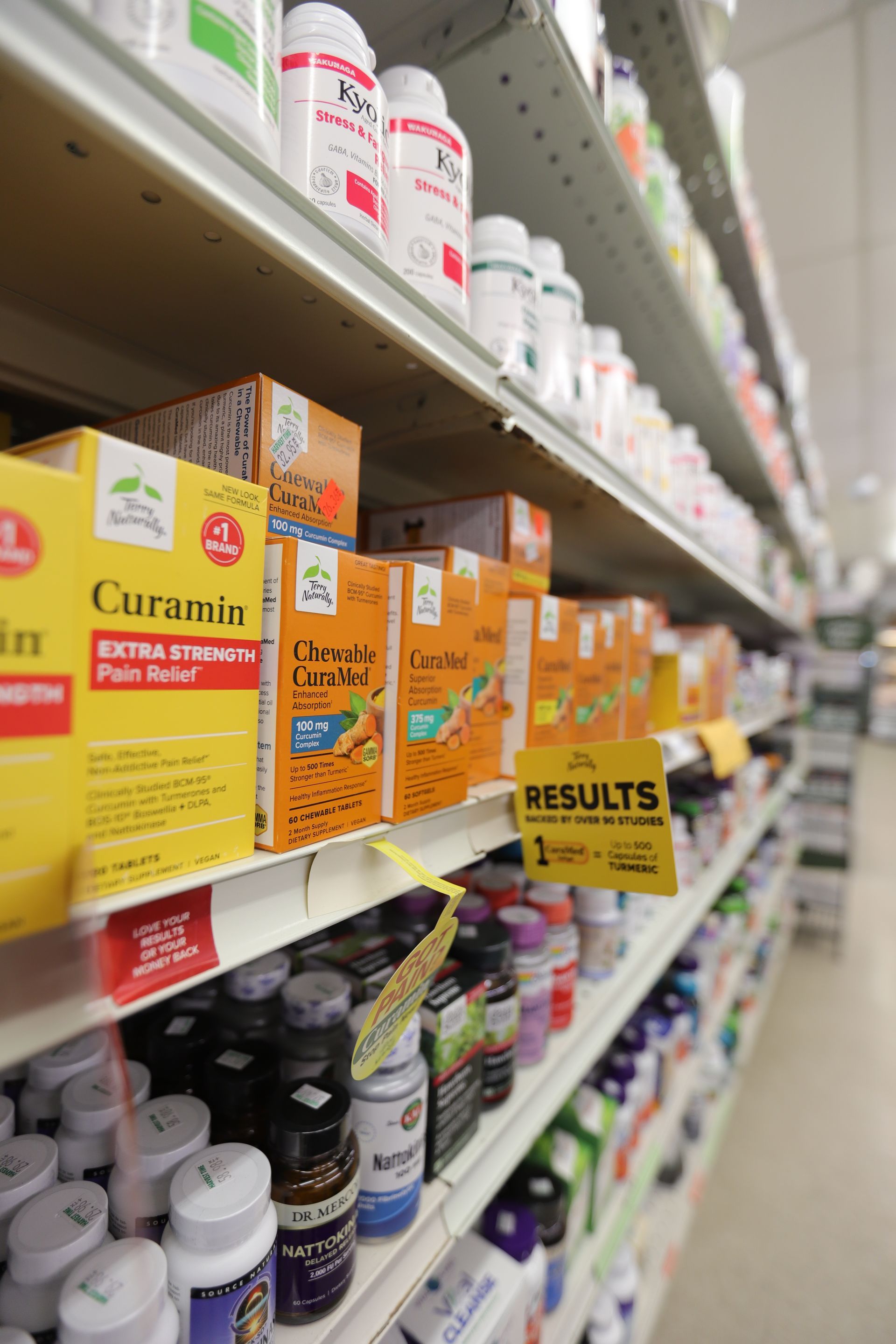A store aisle with shelves stocked with various colorful health supplement bottles and yellow branded boxes.