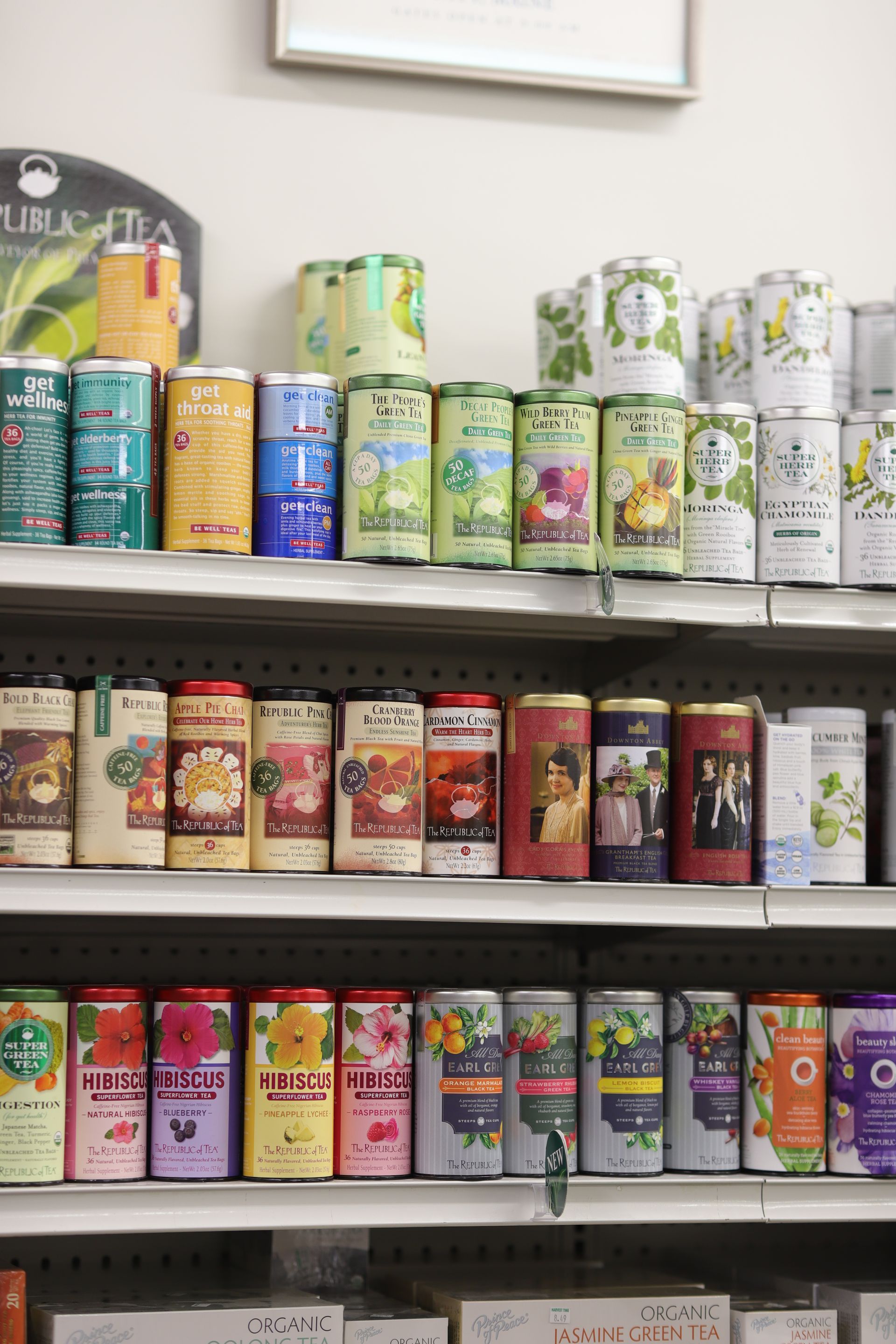 Three shelves in a store stocked with rows of colorful, cylindrical tea tins featuring floral and patterned designs.