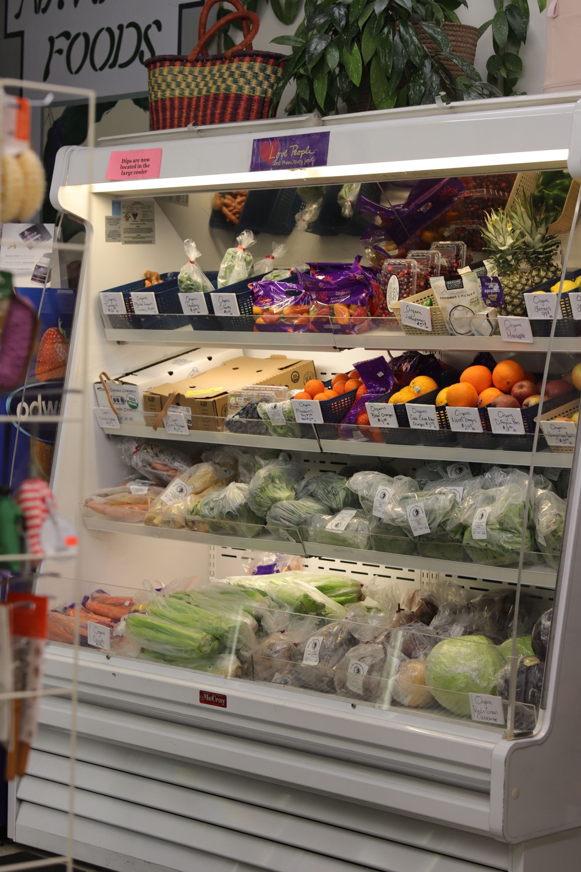 A refrigerated grocery display case stocked with various fresh fruits, vegetables, and packaged produce items.