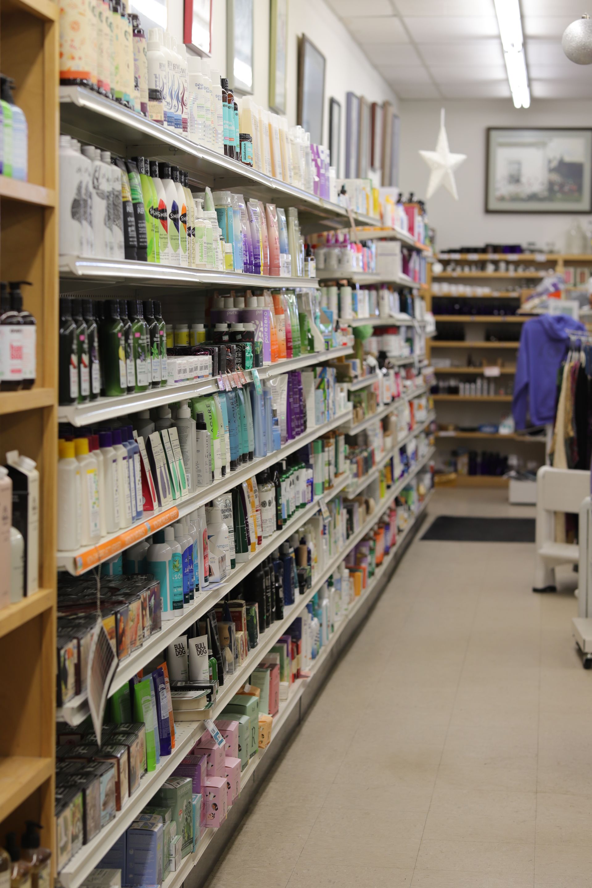 A long, narrow store aisle stocked with rows of various beauty and hair care products on multiple wooden shelves.
