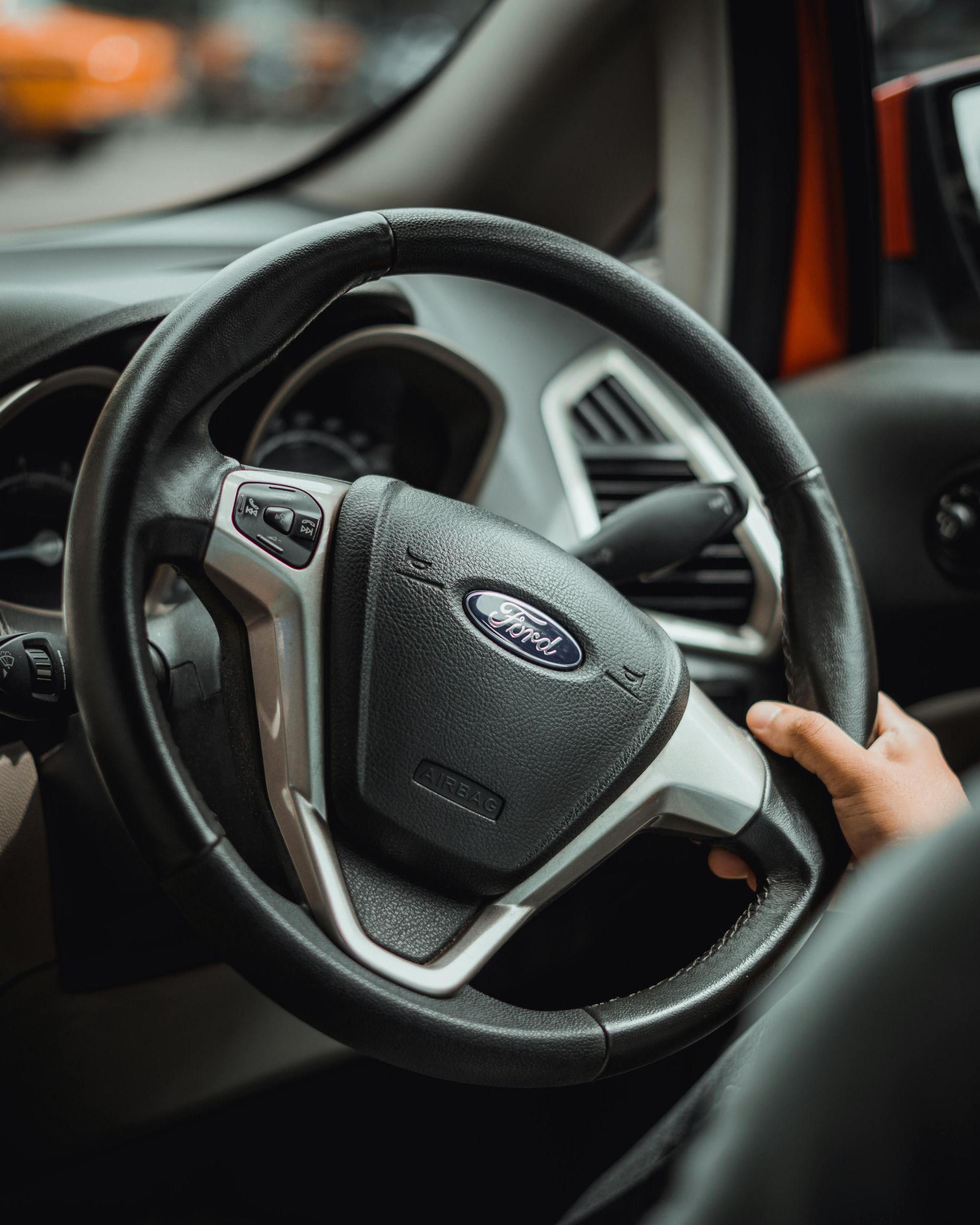 Close-up of a car steering wheel with a hand holding it inside the vehicle