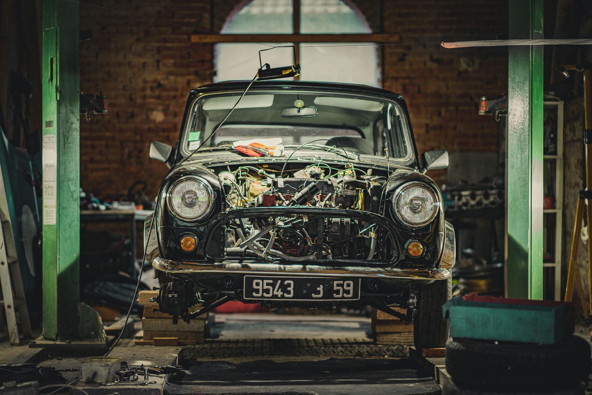 Vintage black car in a garage, front hood open and engine exposed, with tools and equipment around it