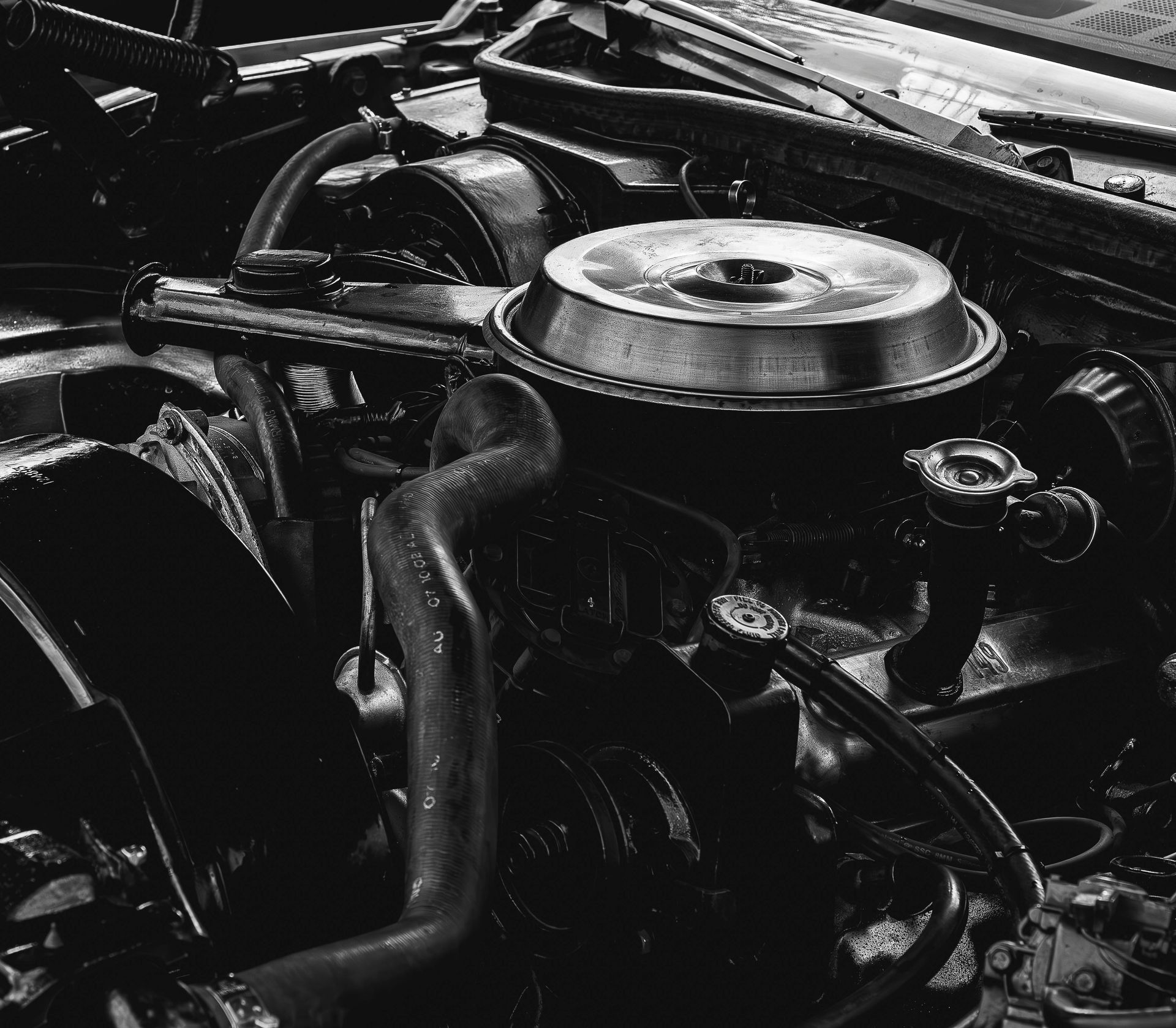 Close-up of a car engine with a round air filter and black hoses in the engine bay