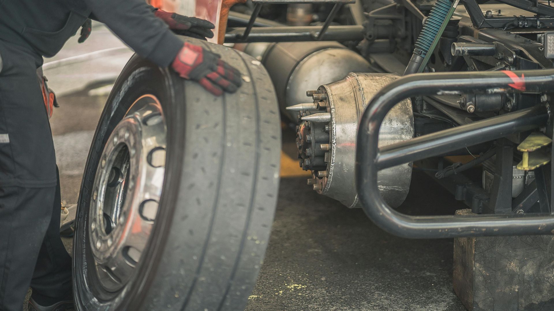 A race car mechanic adjusts a large tire on a stripped-down vehicle in a garage.