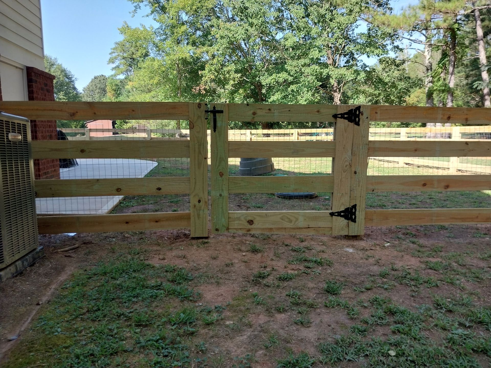 Wooden fence and gate blocking a dirt path in a grassy yard, with trees and a building in the background