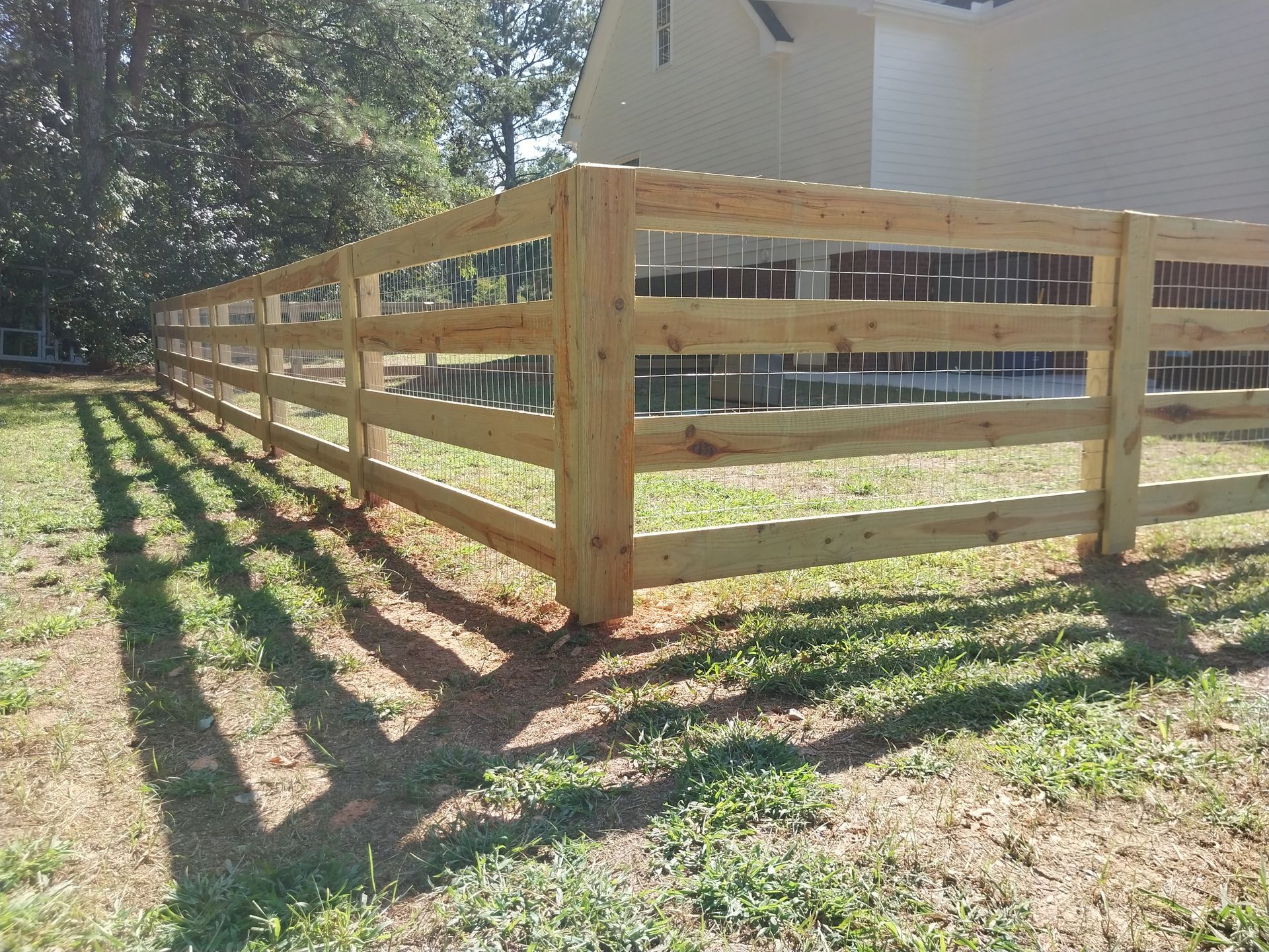 Wooden fence with horizontal rails surrounding a yard in a sunny outdoor setting.