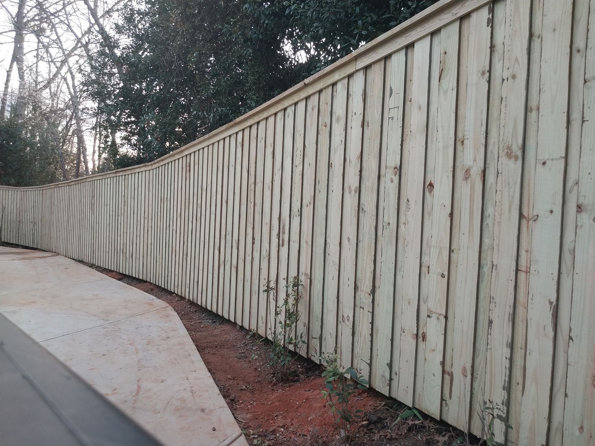 Long white wooden fence lining a curved sidewalk beside a red mulch bed and trees