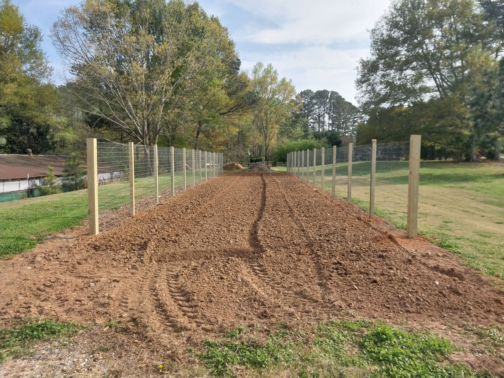Mulched garden bed bordered by posts, with a winding center path in a grassy park-like area