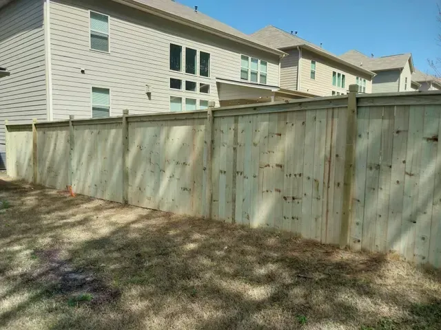 Wooden privacy fence in a grassy yard with apartment buildings behind it under a blue sky