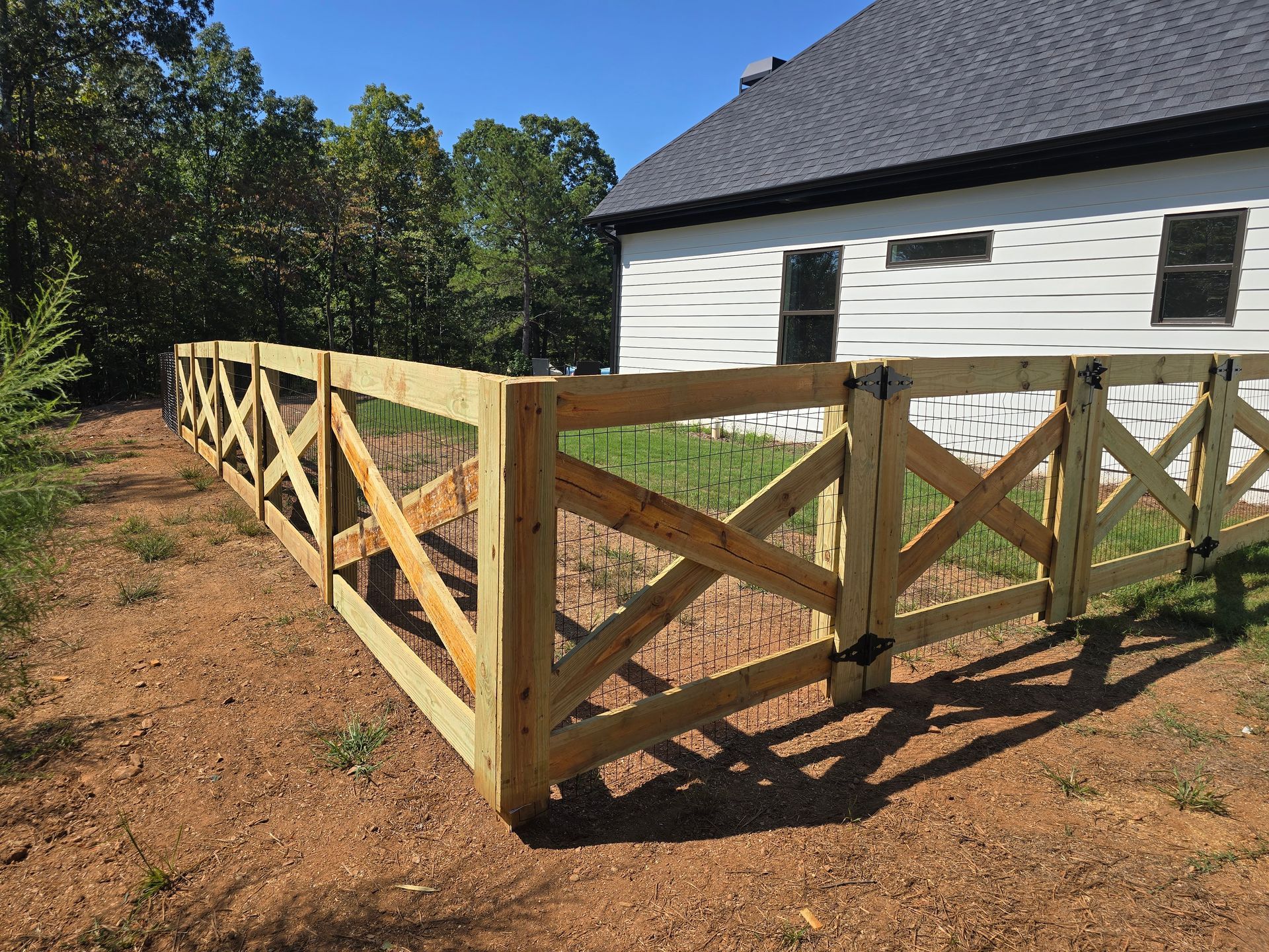 Wooden lattice fence surrounding a white house with a dark roof on a sunny day