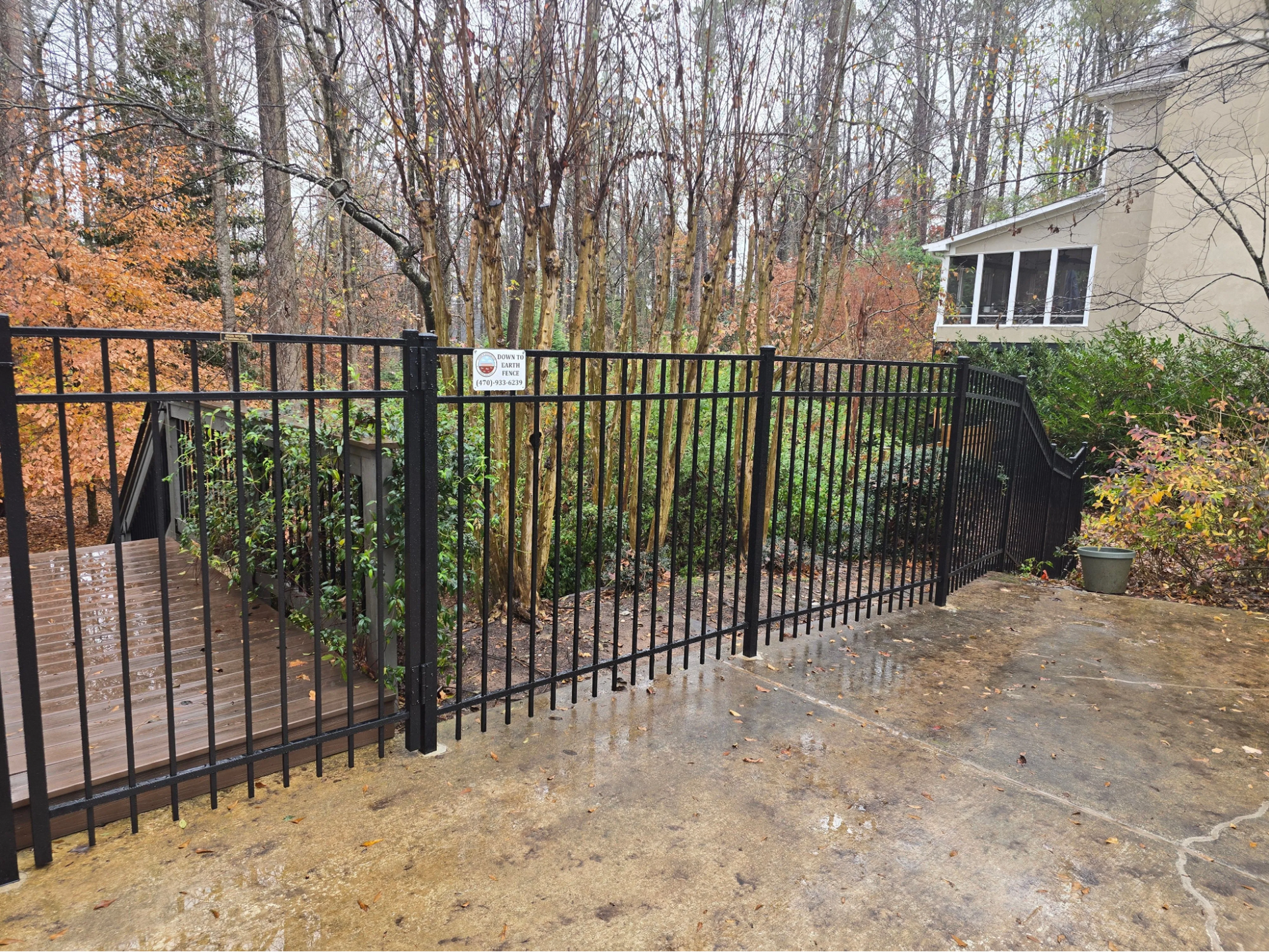 Black metal fence along a wet driveway beside a house and wooded yard