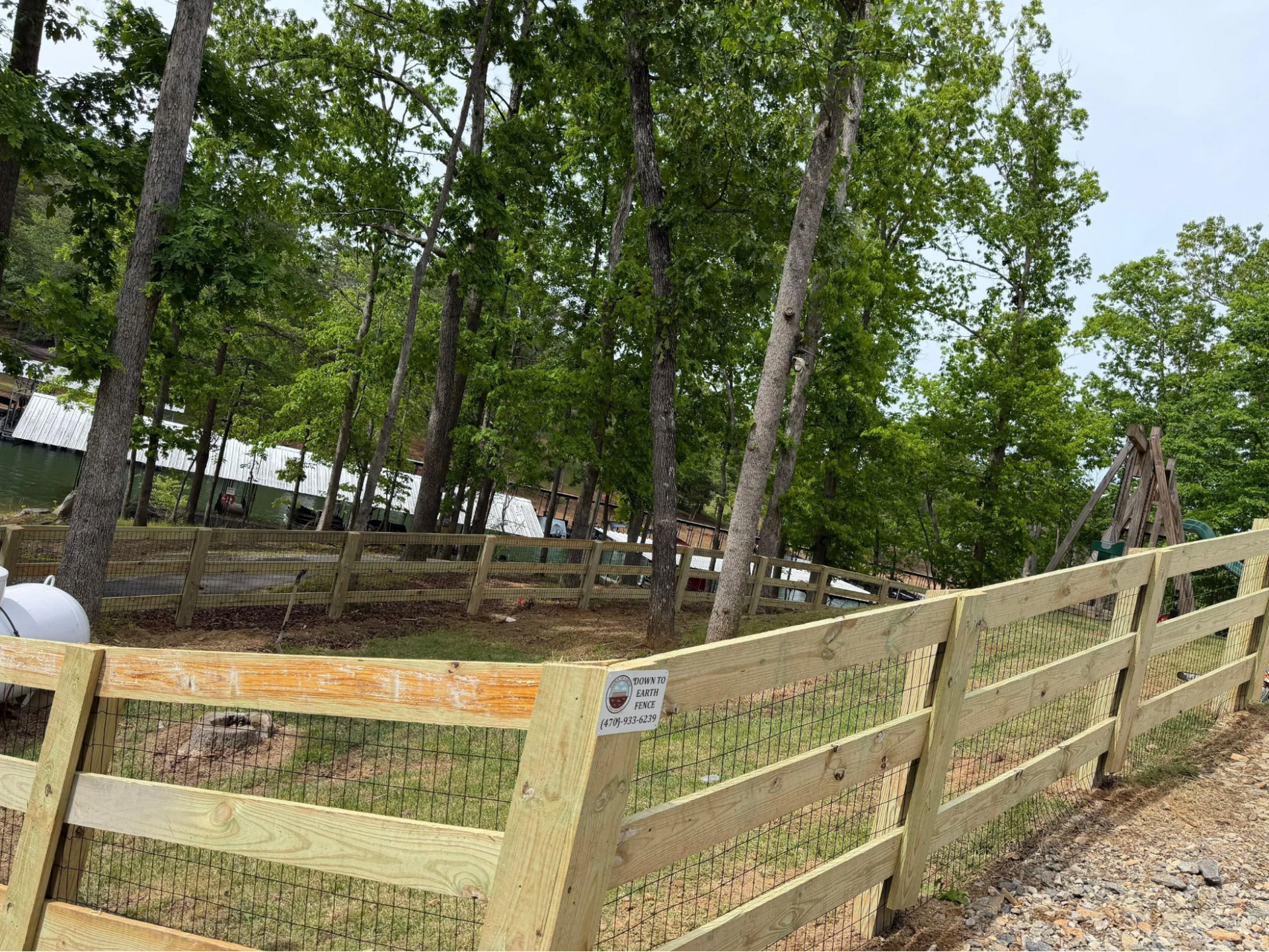 Wooden fence beside a wooded hillside with rocks and a gravel path