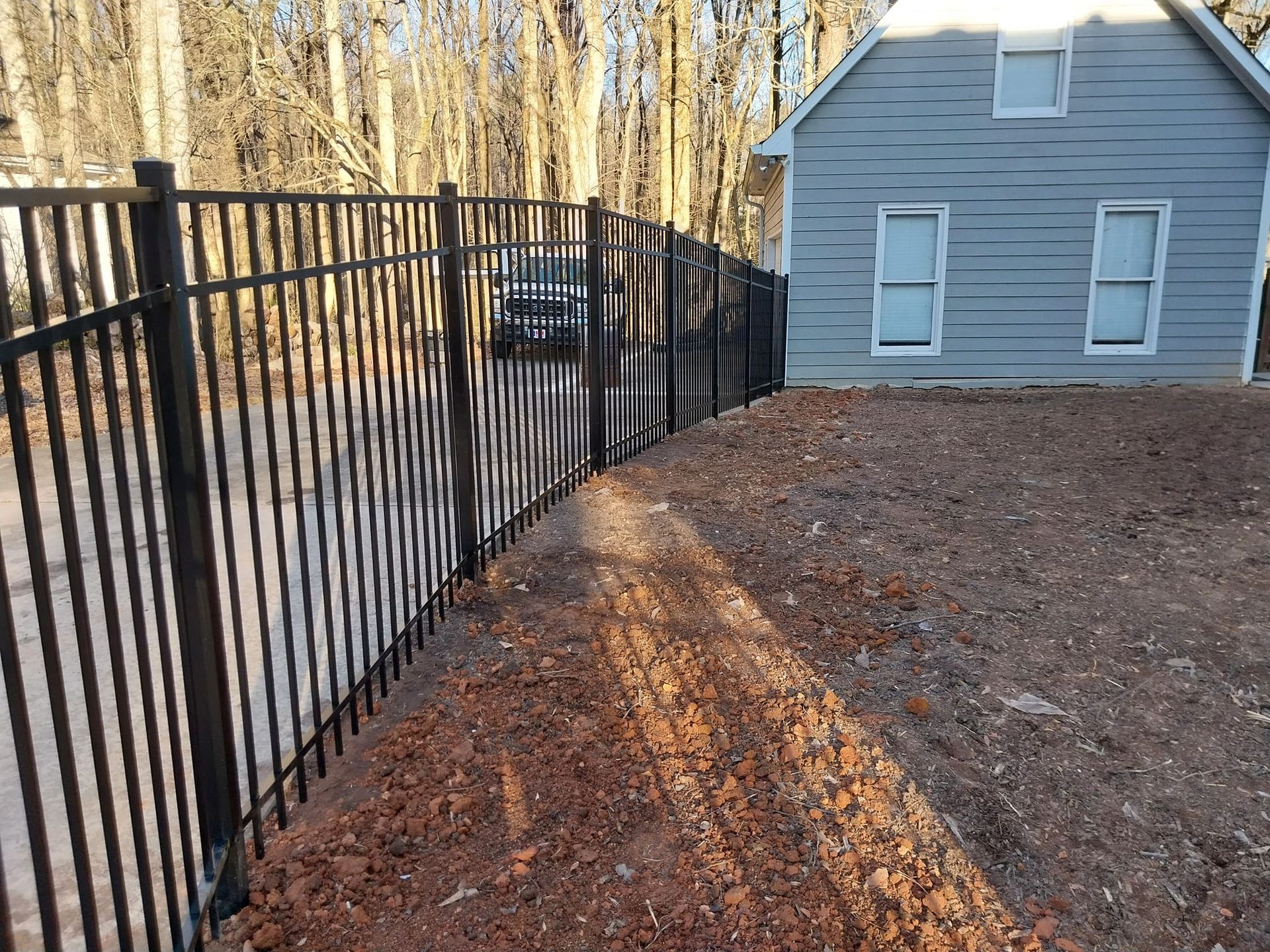 Black metal fence beside a gravel yard and gray house in a wooded area