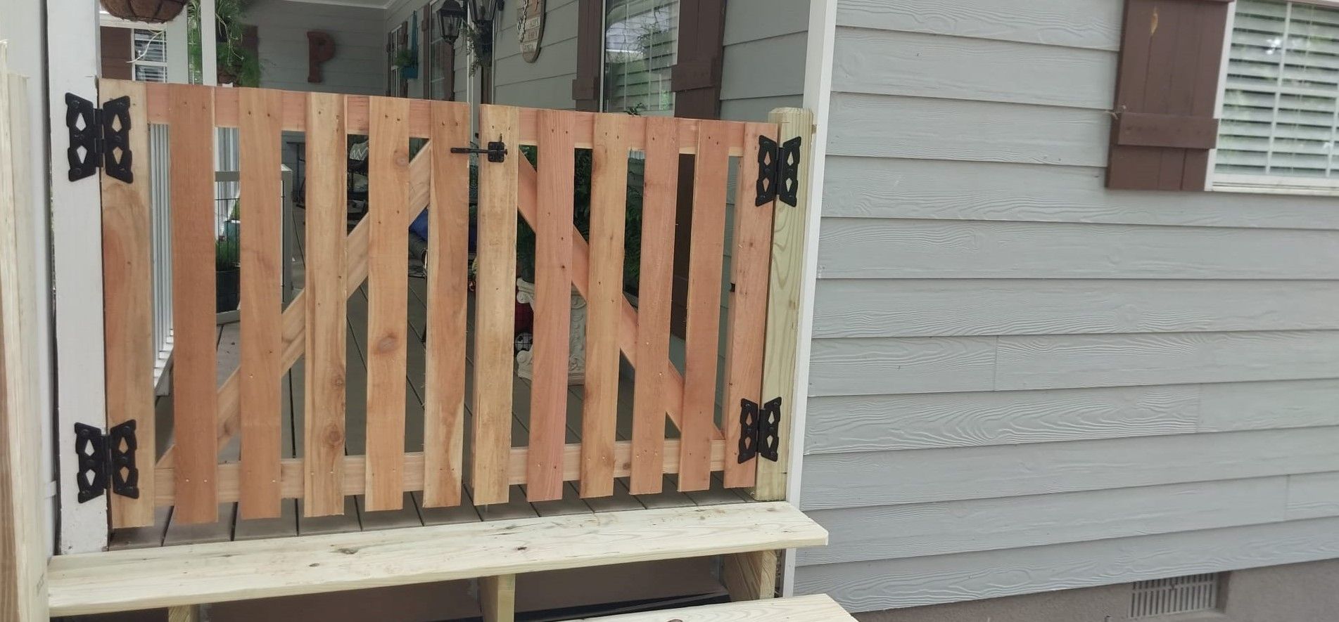 Wooden gate with diagonal slats on a small porch beside a gray house siding