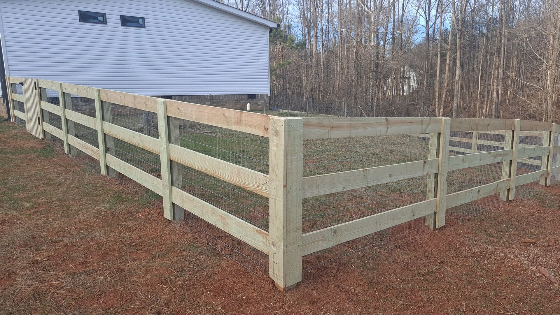 White wooden fence enclosing a grassy yard beside a house with brown leaf-covered ground