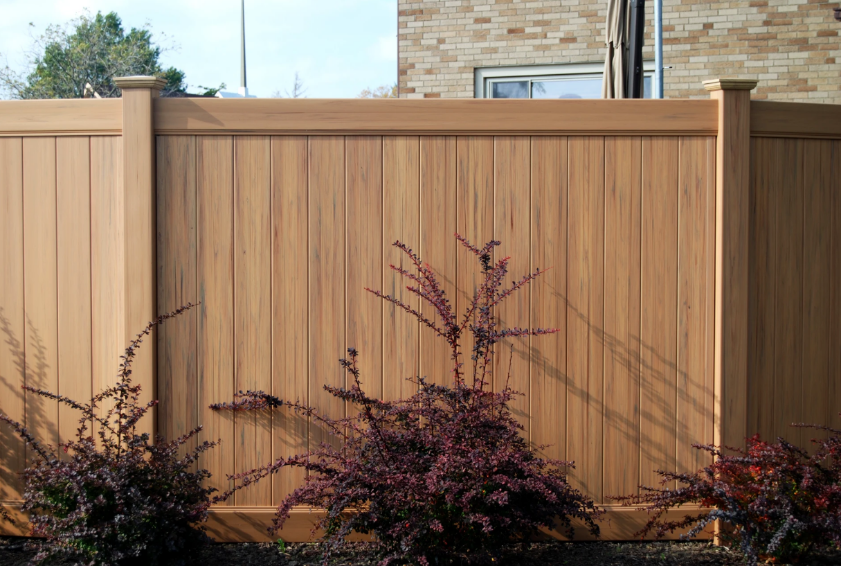 Wooden privacy fence with tan posts and purple shrubs in front, under a clear sky.