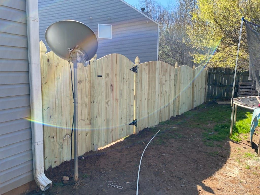 Backyard with wooden fence, satellite dish, house siding, and hose on dirt ground in sunlight