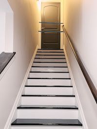 Stairway leading up to a closed black door. White steps with black treads, wooden handrail on the right.
