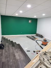 Room under renovation; dark wood-look flooring being installed. Green accent wall, white walls, and ceiling with recessed lights.