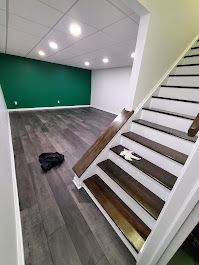 Basement with dark wood floors, white walls, green accent wall, and wooden staircase.