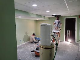 Two people painting a room, one on a ladder, the other on the floor. Light green walls, unfinished floor.
