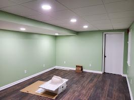 Empty room with green walls, brown floor, and white ceiling with recessed lights. White door visible.