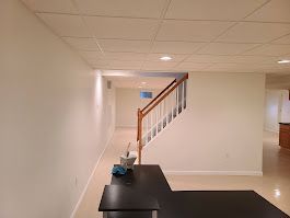 White-walled interior with stairs, recessed lighting, and a dark desk. The ceiling is tiled.