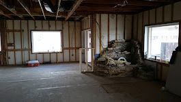 Interior of a room under construction, with exposed framing, two windows, and a rock feature.