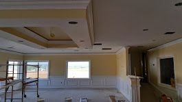 Interior room under construction, with yellow walls, white trim, and a coffered ceiling.