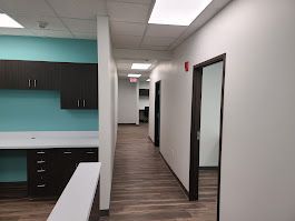 Hallway with brown wood floor, white walls, and dark brown doors. Teal and white workspace on the left.