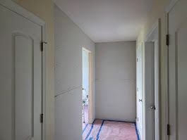 Hallway with three white doors and light gray walls. Pink and blue covering on the floor.