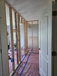 Interior view of a hallway under construction, with exposed wooden studs and a partially built wall.