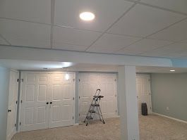 Basement interior with white doors, drop ceiling, and stepladder.