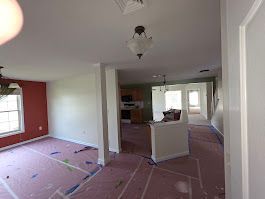 Interior of a home under renovation, with red and white walls, exposed floors, and a view into the kitchen.